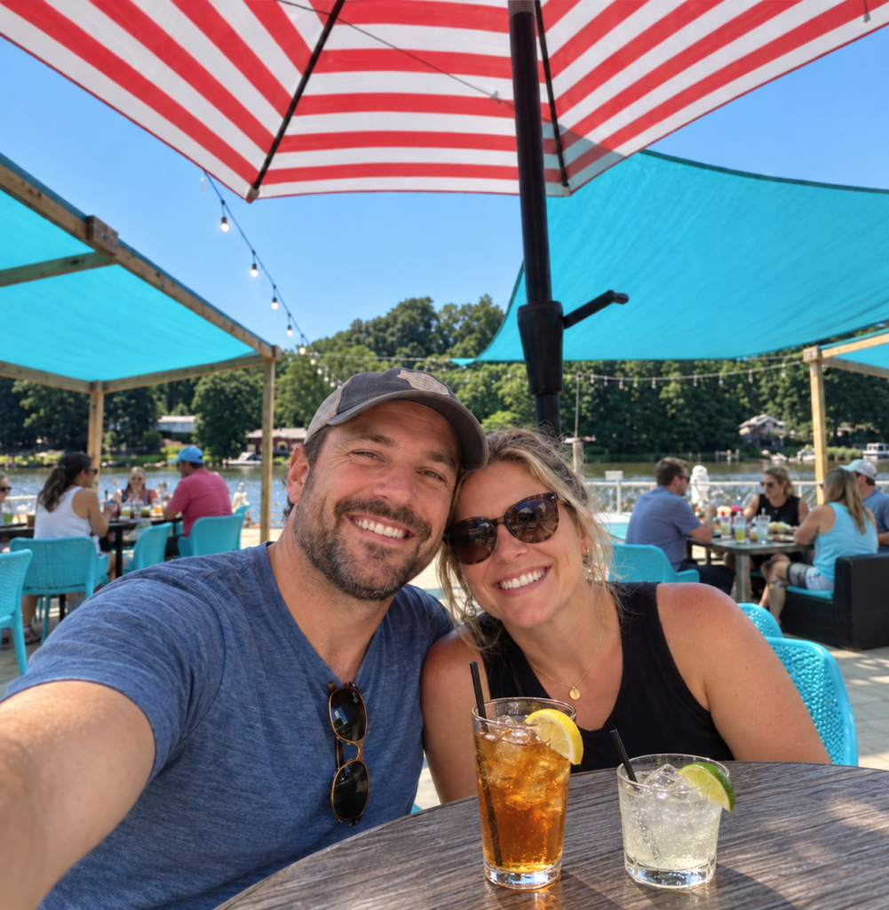 Couple taking a selfie at an outdoor waterfront restaurant patio in Southwest Michigan, with diners seated behind them